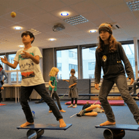 Zwei Jungen stehen auf einem Rola-Bola Balancierbrett. Einer der Jungen jongliert dabei.