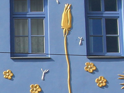 Die blaue Hausfassade der Butterblume bemalt mit goldenen Butterblumen.