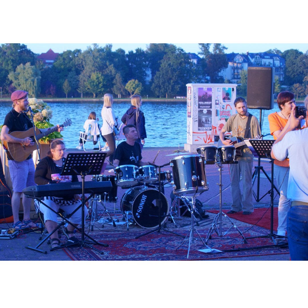 Eine Band musiziert gemeinsam am Rostocker Stadthafen. Im Hintergrund ist die Warnow zu sehen.