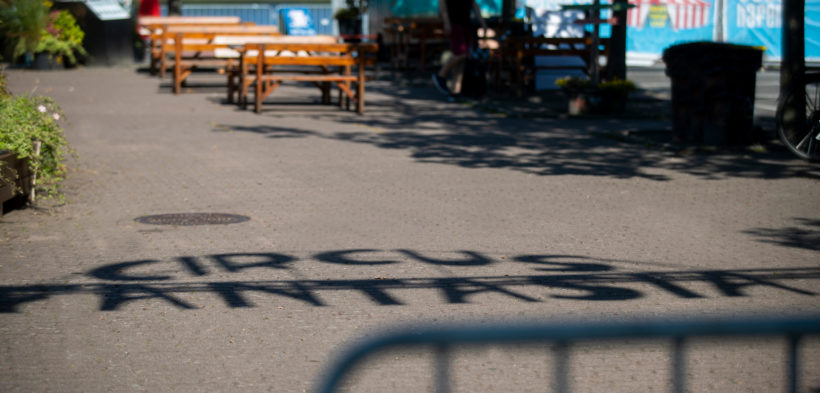 Der Schriftzug "Circus Fantasia" wird als Schatten auf den Boden des Circusplatzes geworfen.