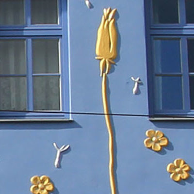 Die blaue Hausfassade der Butterblume bemalt mit goldenen Butterblumen.