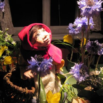 Rotkäppchen als Puppe, die zwischen Blumen in einem Korb sitzt