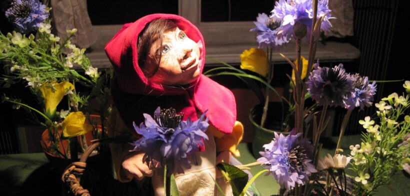 Rotkäppchen als Puppe, die zwischen Blumen in einem Korb sitzt