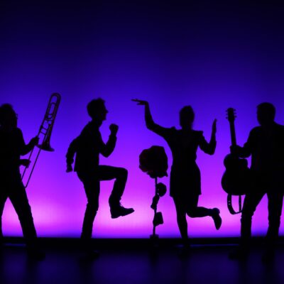 Als Schatten dargestellte Menschen, die tanzen und Instrumente spielen vor einem lila-dunkelblauem Hintergrund