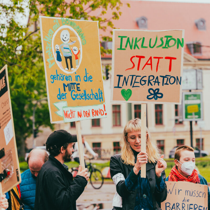 Menschen demonstrieren mit Schildern für Inklusion und Teilhabe in der Rostocker Innenstadt