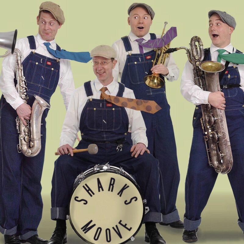 Vier Männer in blauen Latzhosen mit Schiebermütze gucken freudig erstaunt und halten ihre Pauke / Trompete / Posaune / Tuba in der Hand