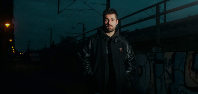 Fotografie von einem Mann in dunkler Kleideung vor Bahnschienen bei Nacht