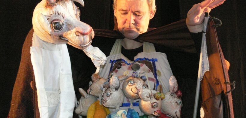 Ein Mann hält eine Ziegenpuppe in der Hand, in seinem Schoß sitzen die kleinen Geißlein