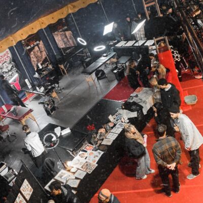 Fotografie des Circuszeltes von Innen, Personengruppen laufen umher, schauen sich Kunst an, manche Menschen werde tätowiert