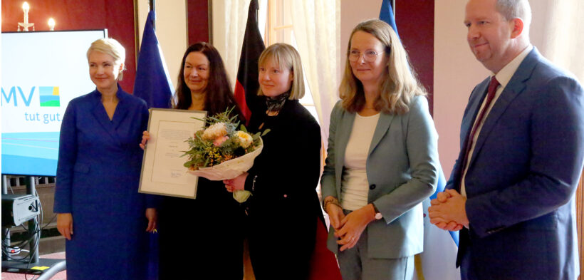 Zwei Mitarbeiterinnen von Fantasia stehen mit Urkunde und Blumenstrauß in der Mitte, daneben stehen Abgeordnete vom Land MV