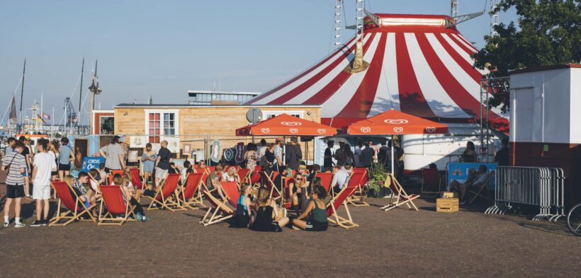 Liegestühle unter sonnigem Himmel, dahinter das weiß-rote Circuszelt
