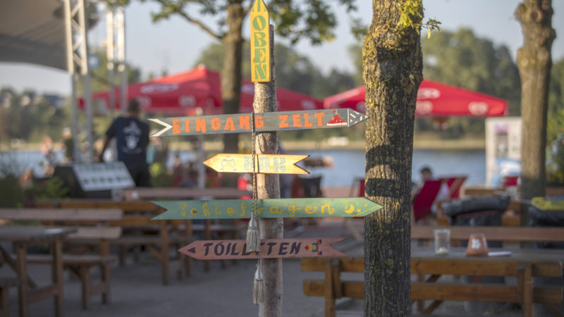 Ein Wegweiser steht auf dem Circus Fantasia Platz und zeigt wo die Toiletten, Schlafwägen, die Bar und der Zelteingang zu finden ist.